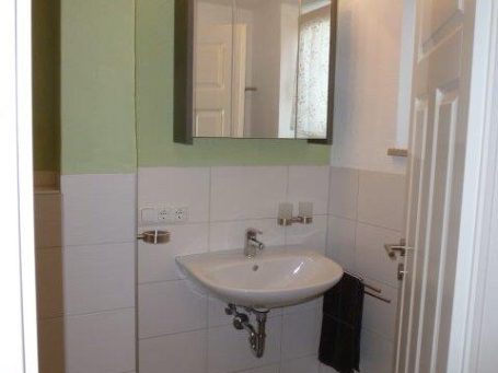 Kleines Bad mit weißem Waschbecken, Spiegel und grünem Farbakzent an der Wand.