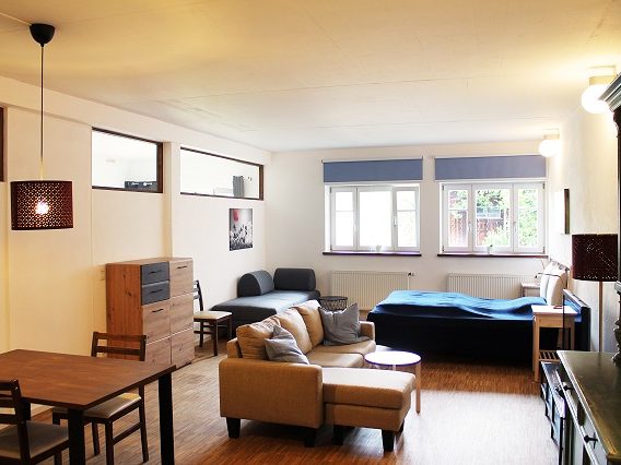 Helles Wohnzimmer mit Sofa, Tisch und Stühlen, großen Fenstern und minimalistischem Design.