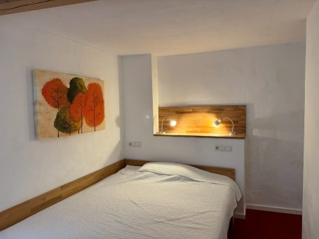 Frei gestaltetes Schlafzimmer mit Doppelbett, holzverkleideter Wand und Kunstwerk.