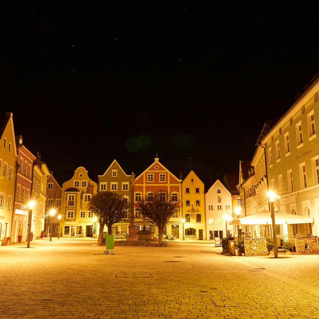 Bunte Fachwerkhäuser und beleuchtete Straßenecken auf einem Platz bei Nacht.