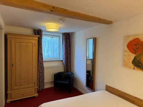 Helles Schlafzimmer mit Bett, Schrank, Stuhl, Spiegel und Fenster.