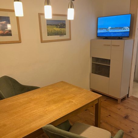 Holzter Tisch mit Stühlen, Fernseher und Bilderrahmen an der Wand in einem Wohnzimmer.