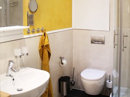 Modernes Badezimmer mit Dusche, Waschbecken, WC und gelbem Handtuch an der Wand.